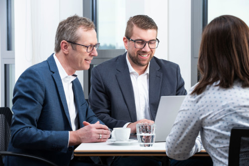 Webdesign Wiesbaden & Online Marketing Agentur – Beratung & digitale Strategien Zwei Berater im Gespräch mit einer Kundin am Tisch, Laptop und Notizen vor sich. Das Bild zeigt eine persönliche Beratung einer Webdesign Wiesbaden & Online Marketing Agentur.